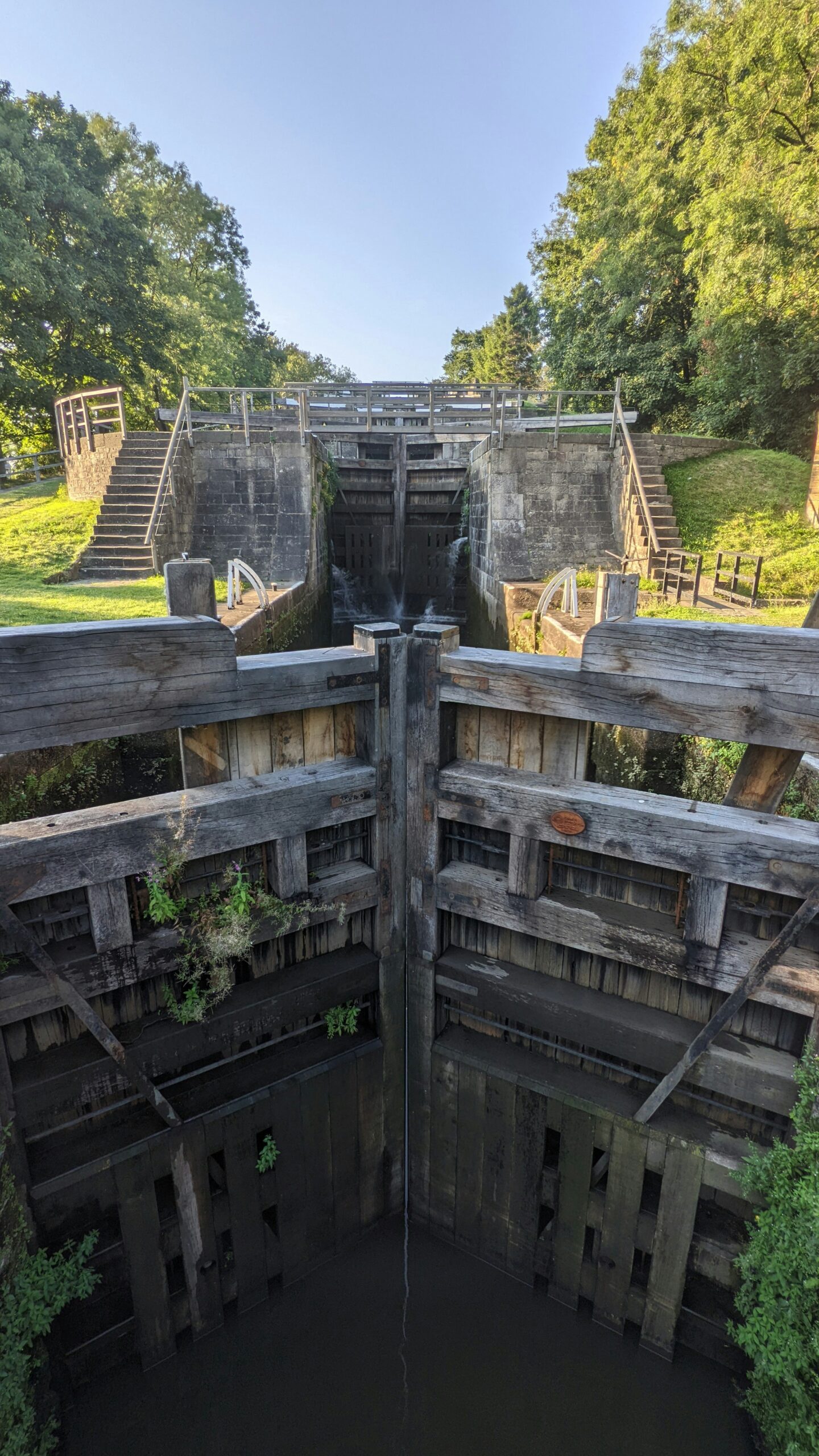 View of the Five Rise Locks in Bingley, featuring a series of five consecutive locks with surrounding greenery and clear blue sky.