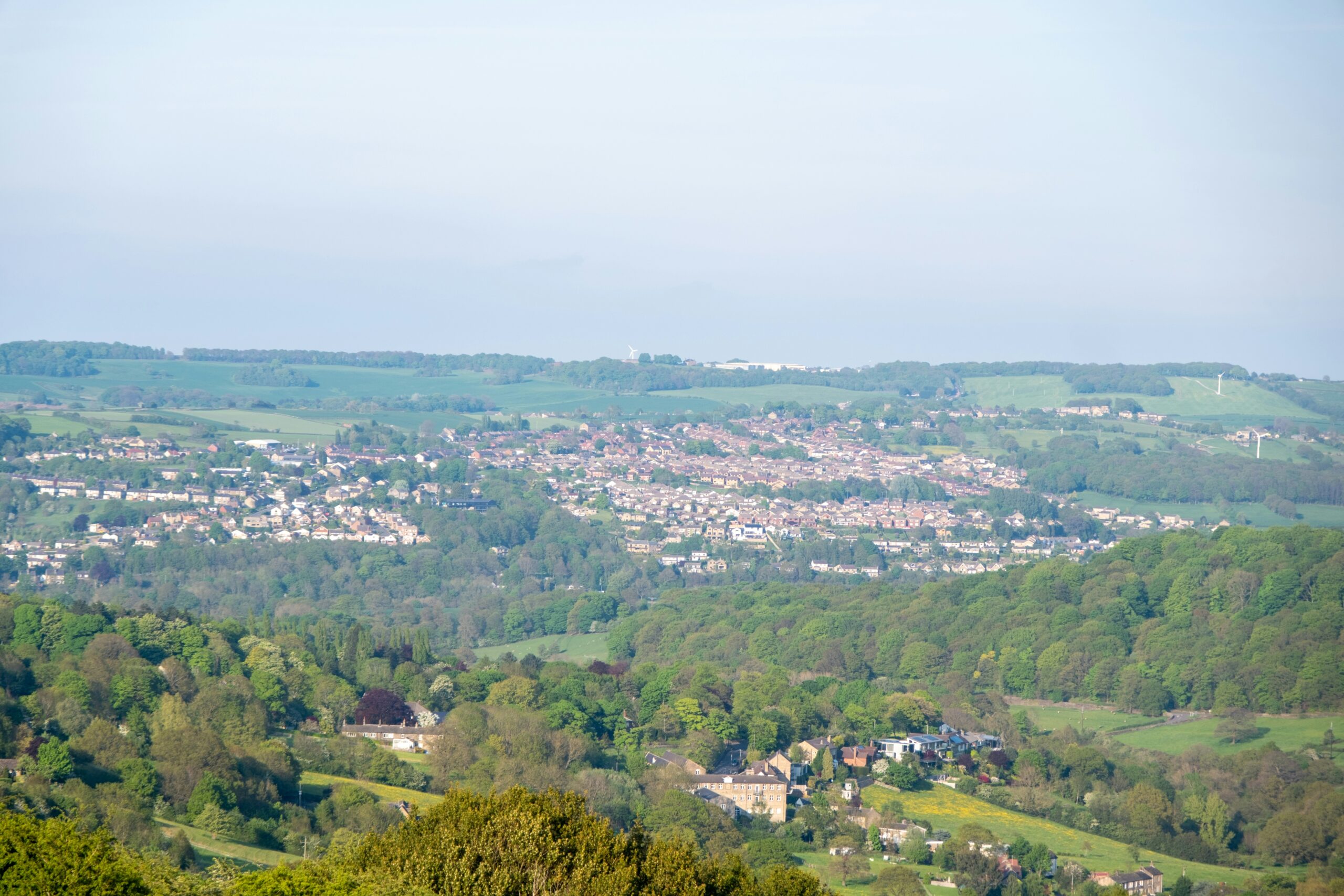 Aerial view of Bingley, showcasing a lush green landscape with rolling hills and a residential area nestled in the valley. 